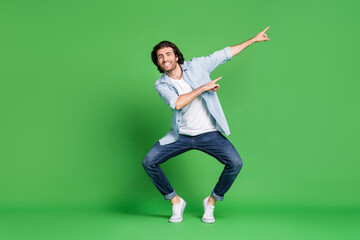Fototapeta na wymiar Full length photo of stubbled man funny legs direct finger empty space wear denim shirt jeans sneakers isolated green color background