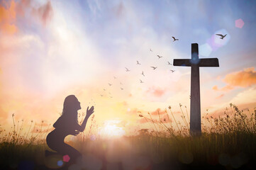 Worship concept: Silhouette woman hand rising for worship God over cross on sunset background