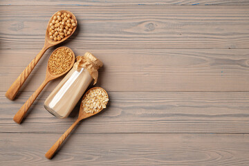 Top view of vegan milk and grains in wooden spoons on wooden surface
