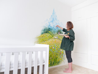Pregnant woman painting a mural on a nursery wall