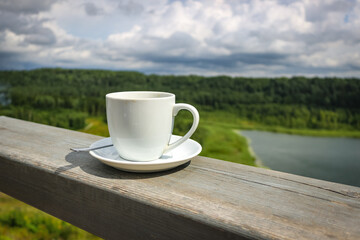 White cup of hot coffee on balcony with natural and mountains, hills background. Copy space.