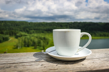 White cup of hot coffee on balcony with natural and mountains, hills background. Copy space.
