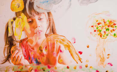 Beautiful young girl painting image on the glass with colorful finger.