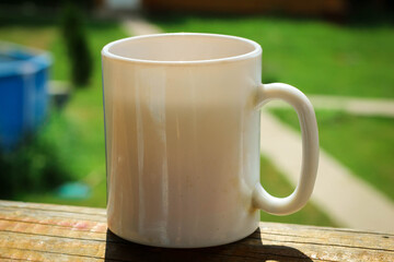 A white cup of tea on the railing of the Wooden terrace. Morning concept. Close-up.