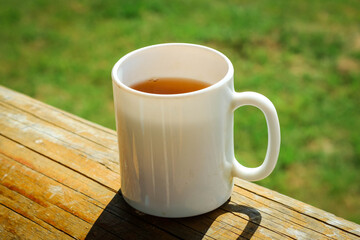 A white cup of tea on the railing of the Wooden terrace. Morning concept. Close-up.