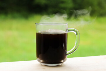 A glass transparent cup with black coffee, from which steam is rising.