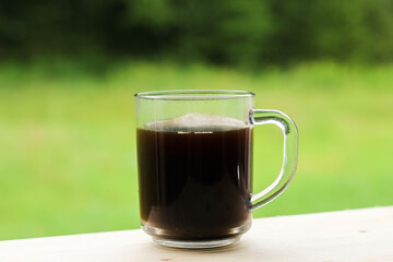 A glass transparent cup with black coffee, from which steam is rising.