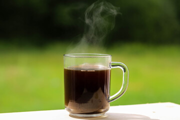 A glass transparent cup with black coffee, from which steam is rising.