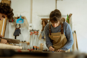 A young female carpenter working as wood designer in a small carpentry workshop. Young business woman handcrafting a piece of timber and designing new house furniture. Entrepreneurs concept lifestyle