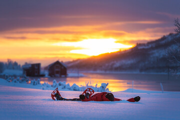 A man with snowshoes under moody sky winter sunset blue hour over the red houses in Norway