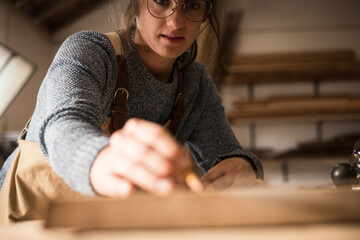 A young female carpenter working as wood designer in a small carpentry workshop. Young business woman handcrafting a piece of timber and designing new house furniture. Entrepreneurs concept lifestyle