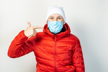 young man points a finger to a medical mask on his face on a light background. Concept of the common cold, virus, infectious diseases