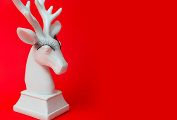 white deer with false eyelashes on red background, minimal creative concept of Christmas and New Year