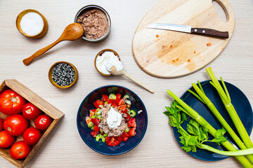 Salad with celery, tomatoes and tuna. Salad ingredients in the cooking process on a light wooden table top view