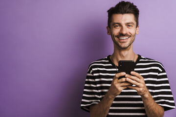 Photo of joyful unshaven man smiling and using cellphone