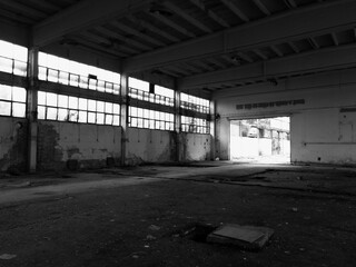 Interior of an abandoned empty industrial hall with broken glass on the windows and peeling walls
