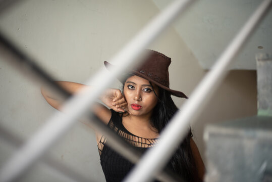 Lifestyle images of young Indian sexy girl in black western dress and cowboy hat on the landing of a staircase with railings as lines. Indian lifestyle