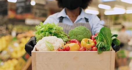 Close up of African American woman hands holding box with vegetables while standing in food store. Female in face mask holding different food in supermarket indoors. Retail concept