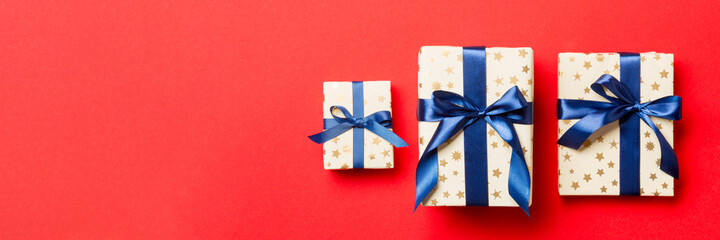 wrapped Christmas or other holiday handmade present in paper with blue ribbon on red background. Present box, decoration of gift on colored table, top view