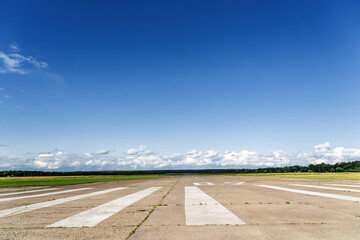 The runway of a rural small airfield against a blue sky with clouds of the airfield. Lonely airfield.