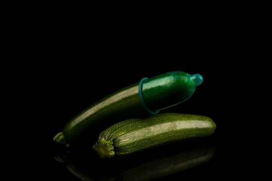 1 gr&uuml;ne Zucchini mit einen gr&uuml;nen Kondom &uuml;berzogen liegt auf einer 2 Zucchini und spiegelt sich im  schwarzen Untergrund in Low Key