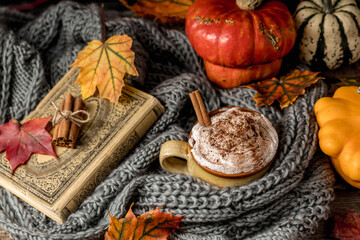 Autumn concept, still life of pumpkin spice latte with whipped milk cream and cinamon. Colorful pumpkins and dry leaves. Old natural wood backround