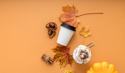 Cozy autumn style flat lay of hot pumpkin spice latte with whipped milk cream, cinamon and colorful dry leaves of october on the light orange background with empty space for logo or design