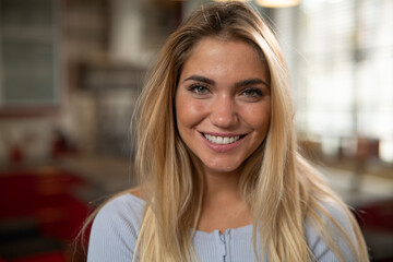 Authentic close up shot of an young blond hair attractive happy woman is smiling in camera in a living room at home.