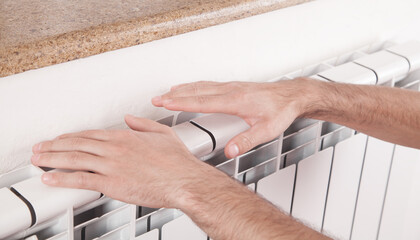 Male hands touch a heating radiator at home.