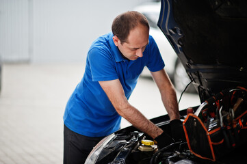 Car repair and maintenance theme. Mechanic in uniform working in auto service, checking engine.