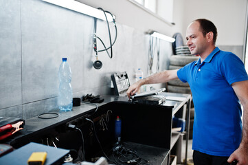 Fototapeta premium Car repair and maintenance theme. Electric mechanic in uniform working in auto service, making car diagnostics using obd device with laptop.