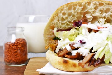 A delicious, fresh kebab from Germany lies on a wooden surface, next to it is an ayran and hot spice - a popular kebab to take away from Germany, the so-called Döner lies ready to eat at the table