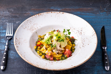 Salad with chicken fillet, sweet corn and fresh vegetables on a plate served with fork and knife