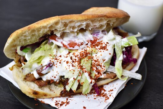 A delicious, fresh kebab from Germany lies on a wooden surface, next to it is an ayran and hot spice - a popular kebab to take away from Germany, the so-called D&ouml;ner lies ready to eat at the table