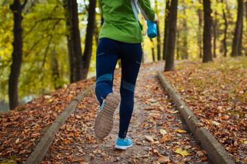 Runner working out in autumn park. Young woman running with water bottle. Active healthy lifestyle. Close up of shoes