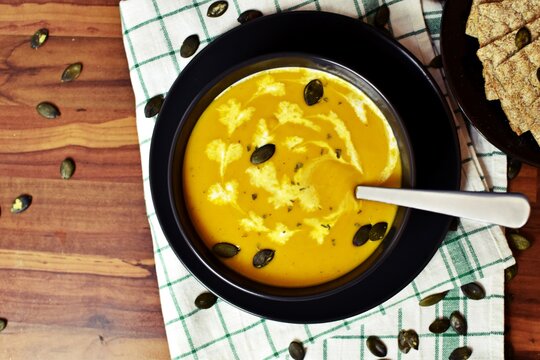 Close-up on a bowl of pumpkin cream soup, a man eating out of it - delicious pumpkin cream soup garnished with pumpkin seeds and cream as a warm snack in the cool and wet autumn