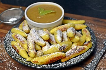 Delicious, fried Schupfnudeln from Germany lie covered with icing sugar next to a bowl of apple sauce. Delicious dessert as a sweet lunch in Germany