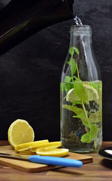 Hot water is poured into a glass bottle containing slices of lemon and mint - homemade tea as refreshment in summer with mint and lemon on one surface - background with homemade tea