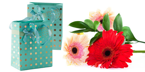 Obraz premium Turquoise paper bag with satin ribbon handles for gift wrapping with a bouquet of gerbera flowers, isolated on a white background,copy space