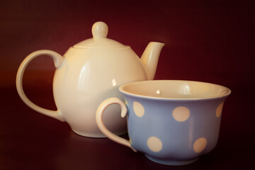 Porcelain kettle with tea cup, maroon background
