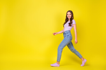 Fototapeta na wymiar Full length body size profile side view of lovely cheerful wavy-haired girl walking copy space isolated over bright yellow color background
