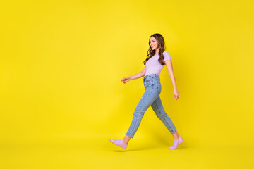 Fototapeta na wymiar Full length body size profile side view of pretty cheerful wavy-haired girl walking isolated over vibrant yellow color background