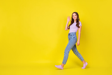 Full length body size profile side view of attractive friendly cheerful wavy-haired girl going waving hi hello isolated bright yellow color background