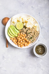 A bowl of healthy vegan and vegetarian lunch or dinner. Salad of fried chickpeas, quinoa, avocado, cauliflower on a light background.Top view, flat lay