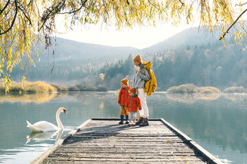 Family in nature background. Woman and children looking at swan in lake.