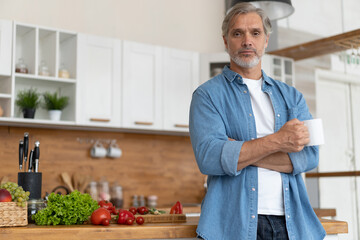 Grey-haired Mature handsome caucasian man standing in the bright kitchen.