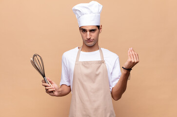 young baker man making capice or money gesture, telling you to pay your debts!