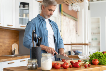 Grey-haired Mature handsome man preparing delicious and healthy food in the home kitchen