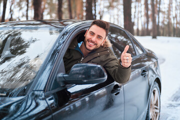 Young attractive Caucasian man sits at the wheel of his car sunny winter day.