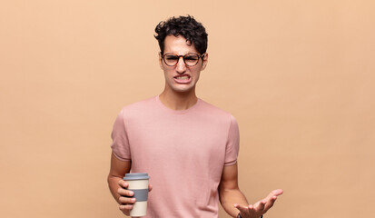 young handsome man with a coffee looking angry, annoyed and frustrated screaming wtf or what’s...